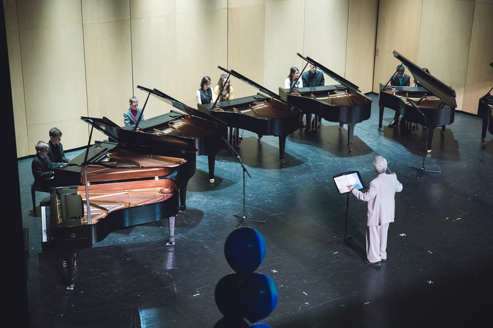 A group of pianos with a director leading the players.