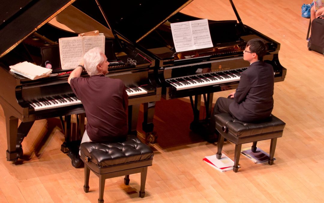 A piano teacher talking with a student on another piano.